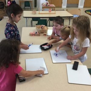 5 preschool children around a table drawing on dry erase boards